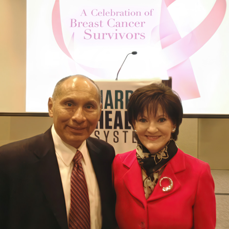 David Lopez in a suit posing with keynote speaker Beth Sanders Moore in a hot pink jacket at a Harris Health breast cancer survivor celebration.