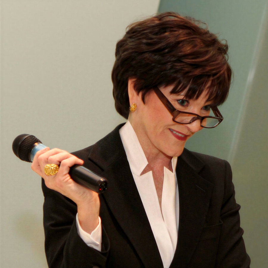 Keynote speaker Beth Sanders Moore wearing glasses and black suit with a mic in her hand at a MD Anderson Cancer Survivorship symposium.